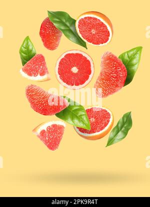 Tasty ripe grapefruits and green leaves falling on beige background Stock Photo