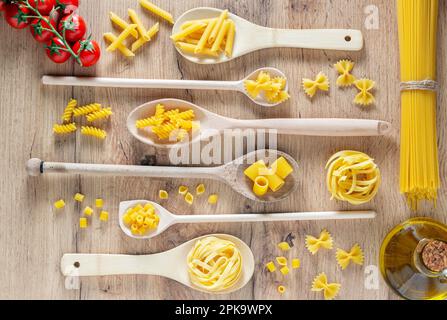 Various pasta in spoons, tomatoes and olive oil. Top view flat lay Stock Photo