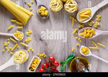 Various pasta in spoons, tomatoes, basil and olive oil. Top view flat lay Stock Photo