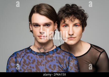 portrait of young and stylish pansexual couple with makeup looking at camera isolated on grey,stock image Stock Photo