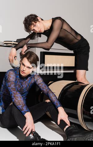 young nonbinary couple in stylish clothes posing near huge model of photo camera on grey background,stock image Stock Photo