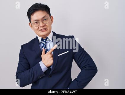 Young asian man wearing business suit and tie pointing aside worried and nervous with forefinger, concerned and surprised expression Stock Photo
