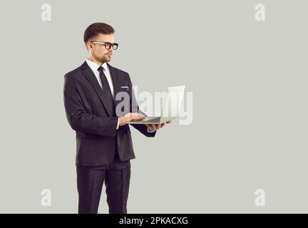 Serious businessman standing isolated on gray background and working on laptop computer Stock Photo
