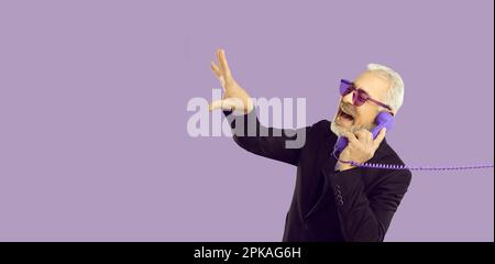 Cheerful and stylish senior man talking on landline phone isolated on pastel purple background. Stock Photo