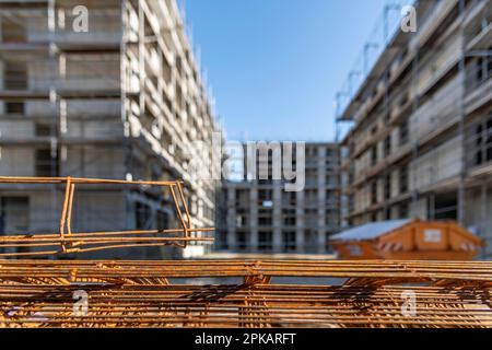 Rusty steel probation lies stacked on the ground at a large construction site with multi-story buildings in the shell in the background Stock Photo