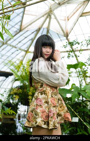 Young Asian Woman in a Tropical Forest Greenhouse | Short Floral Print Dress | Conservatory of Flowers Stock Photo