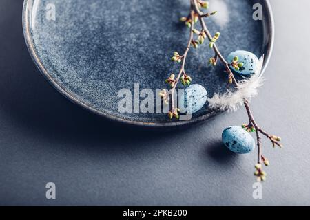 Easter dish decorated with blue eggs, feathers and spring branches. Ceramic plate on grey background. Space. Holiday mockup Stock Photo