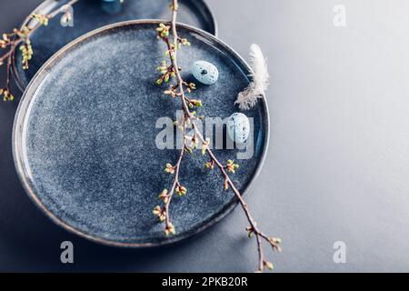 Easter dish decorated with blue eggs, feathers and spring branches. Ceramic plate on grey background. Space. Holiday mockup Stock Photo