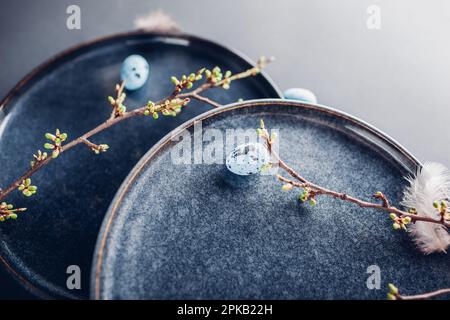 Rustic Easter dishes decorated with blue eggs, feathers and spring branches. Ceramic plate on grey background. Holiday mockup. Top view of vintage pot Stock Photo