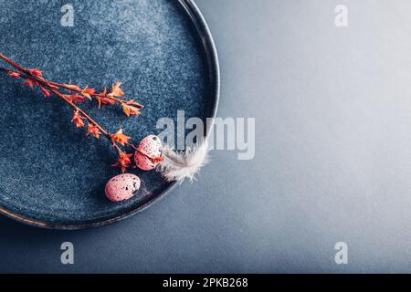 Easter decor. Close up of dishes with eggs, feathers and red spring branches. Ceramic plates on grey background. Space. Holiday mockup Stock Photo