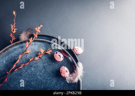 Easter decor. Close up of dishes with eggs, feathers and red spring branches. Ceramic plates on grey background. Space. Holiday mockup Stock Photo