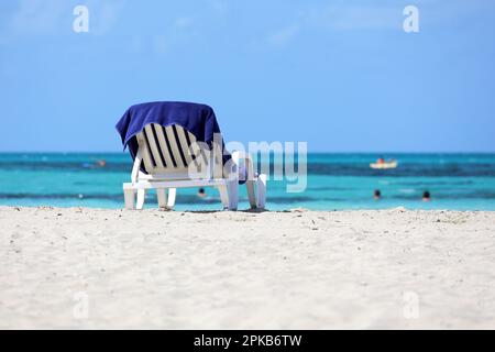 Deck chair with blue towel on sandy beach on swimming people background. Sea resort on Caribbean island Stock Photo