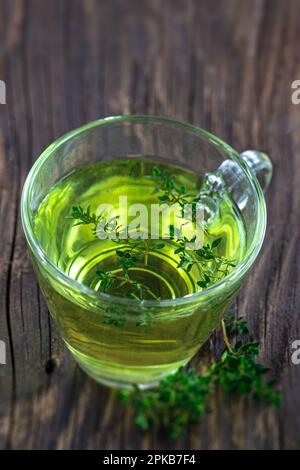 Thyme (thymus vulgaris) herbal tea viewed from above in a glass cup on the background of old board. Stock Photo