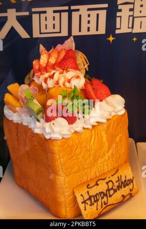 Japan, Honshu, Tokyo, Coffee Shop Window Display of Loaf Topped with Cream and Fruits with Happy Birthday Sign Stock Photo