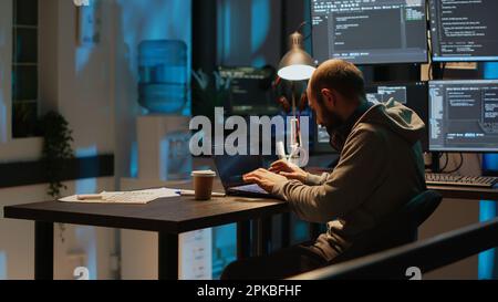 Database programmer typing server code on multiple screens using coding language on laptop late at night. Programming online firewall system on monitors to develop new html script. Stock Photo