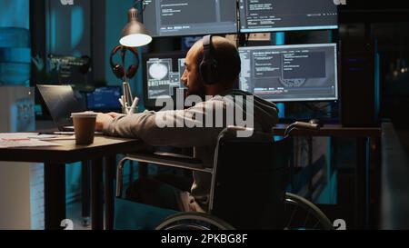 System admin using terminal window on laptop to program new code, dealing with physical impairment. Male web developer in wheelchair coding firewall security or html script. Tripod shot. Stock Photo