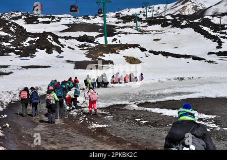 group of people, adult and children of a school, going up the slope of Etna volcano in winter National Park, Sicily, Italy Stock Photo