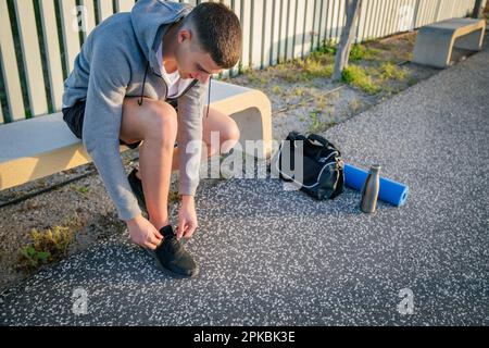 A sportsman sitting on a bench is tying his shoes, photo with copy space Stock Photo
