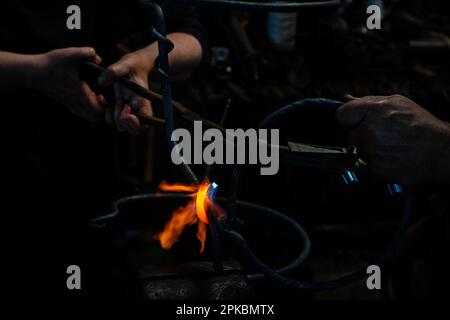 Forge close-up of hands with tongues working on piece, Craftsman forges molten metal on an anvi Stock Photo
