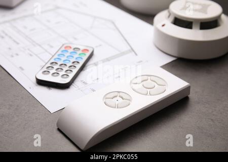 Remote controls, smoke detector and building plan on grey table, closeup. Home security system Stock Photo