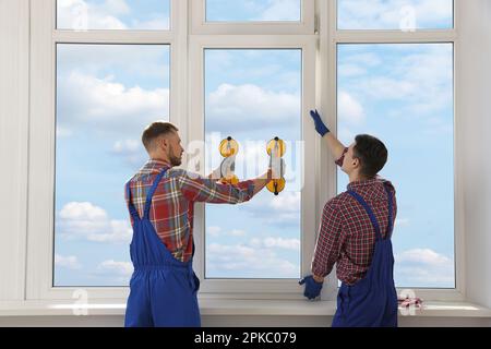 Workers using suction lifters during plastic window installation indoors Stock Photo