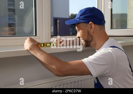 Worker using bubble level after plastic window installation indoors Stock Photo
