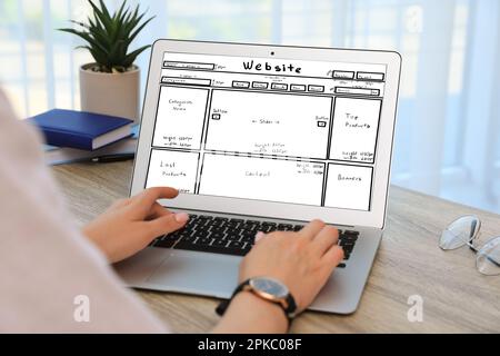 Designer creating website on laptop at wooden table, closeup Stock Photo