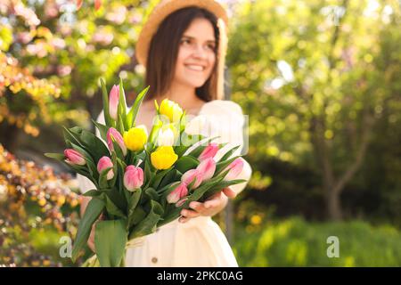 Beautiful young woman with bouquet of tulips in park, focus on flowers. Space for text Stock Photo