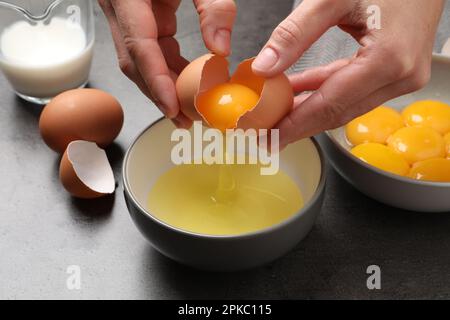 Woman separating egg yolk from white over bowl at grey table, closeup Stock Photo