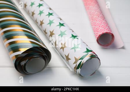 Different colorful wrapping paper rolls on white wooden table, closeup Stock Photo