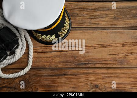 Peaked cap, rope and binoculars on wooden background, flat lay. Space for text Stock Photo