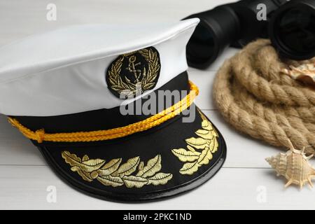 Peaked cap, rope, shells and binoculars on white wooden background, closeup Stock Photo