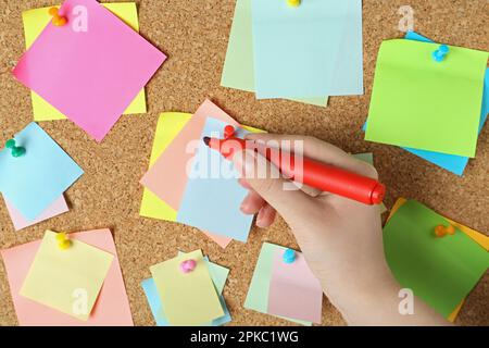 Woman writing on sticky note pinned to corkboard, closeup Stock Photo