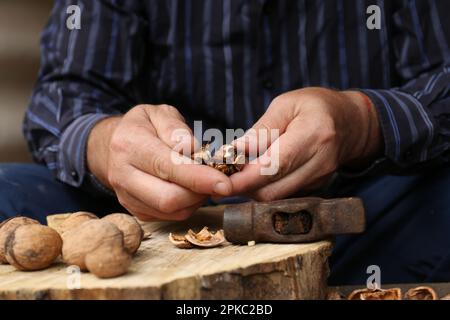 Man cracking walnuts with hammer at table, closeup Stock Photo