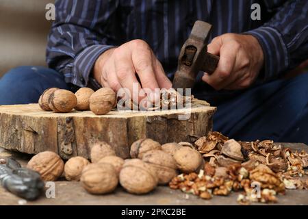 Man cracking walnuts with hammer at wooden table, closeup Stock Photo