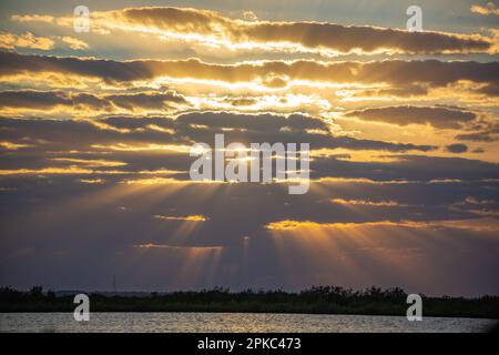 a picture of a cloudy sky and a sunset, the sun rays are glowing through the clouds. Lake and the horizon on the bottom part. Stock Photo