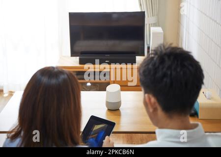 A man and a woman relaxing in the living room with AI speakers placed on the table Stock Photo