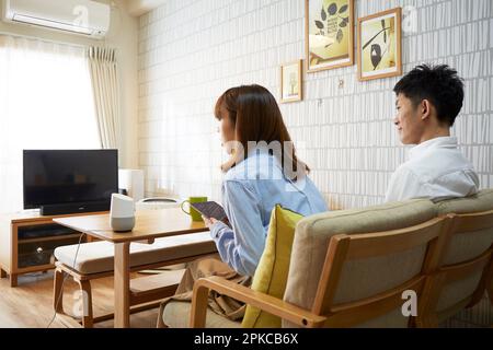 Man and woman relaxing in the living room with AI speakers on the table Stock Photo