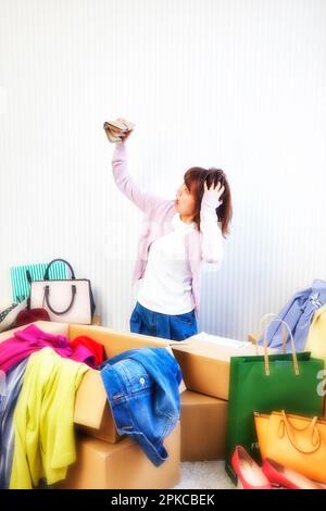 Woman with purse and room cluttered with clothes, bag, etc. coming out of box Stock Photo