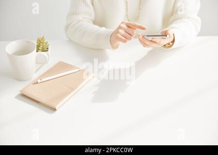 Woman operating a smartphone sitting in front of a desk Stock Photo