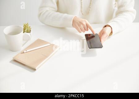A woman operating a smartphone while sitting at her desk Stock Photo