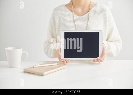 Woman sitting in front of a desk holding a tablet Stock Photo