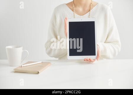 Woman sitting in front of a desk holding a tablet Stock Photo