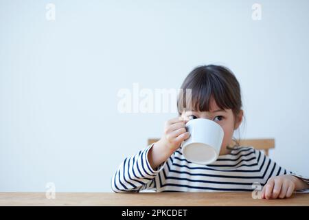 Girl sipping juice in large mug at table Stock Photo