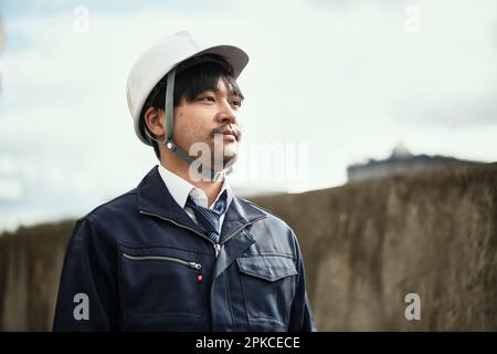 Man in work clothes and helmet looking into distance Stock Photo