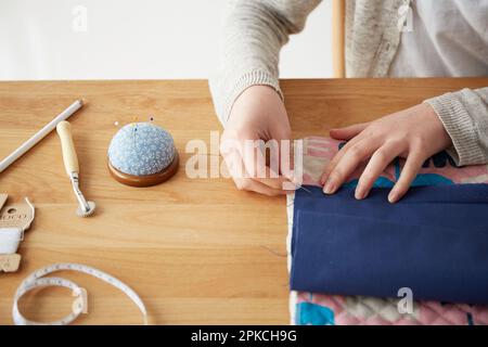 Woman's hand pointing a needle to a cloth on the table Stock Photo