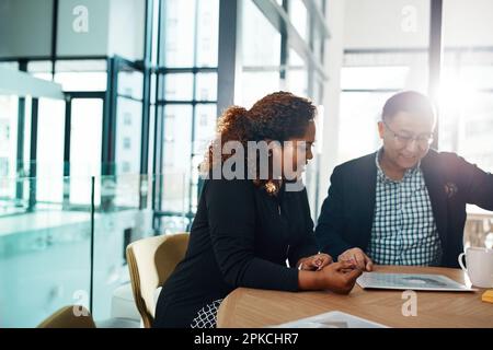 Discussing ways to profit from all their top ideas. two businesspeople going through some paperwork in an office. Stock Photo