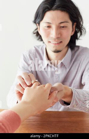 A man putting on an engagement ring and a woman's hand receiving it Stock Photo