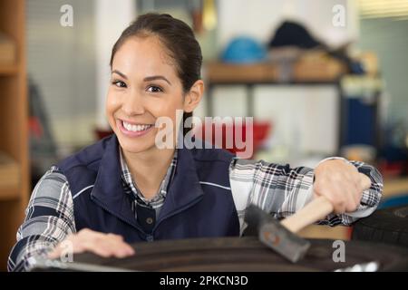 female mechanic using a hammer while working on a tyre Stock Photo