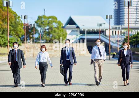 Five office workers walking side by side wearing masks Stock Photo